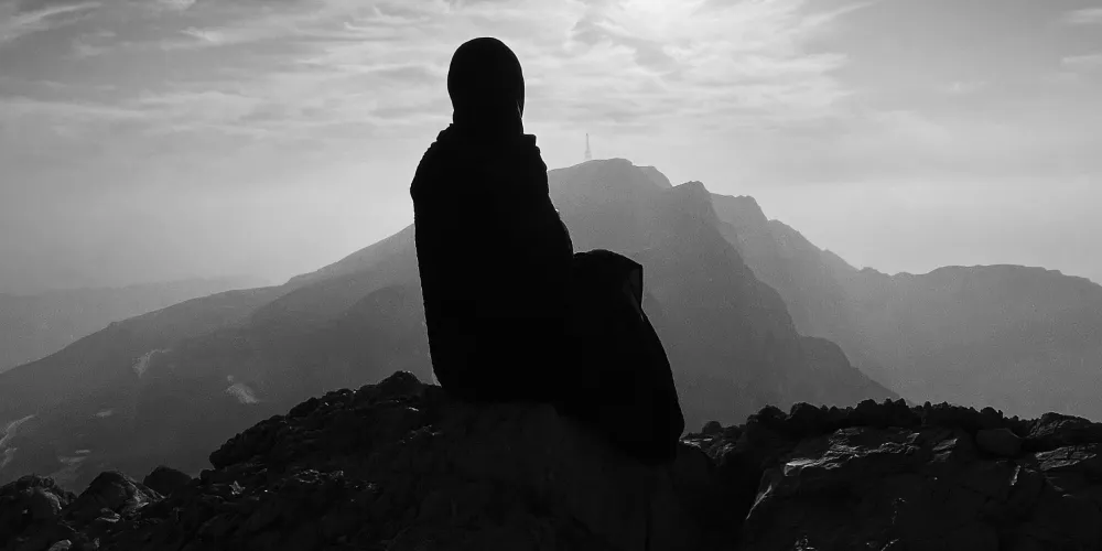 A woman in hijab seated on a mountain peak